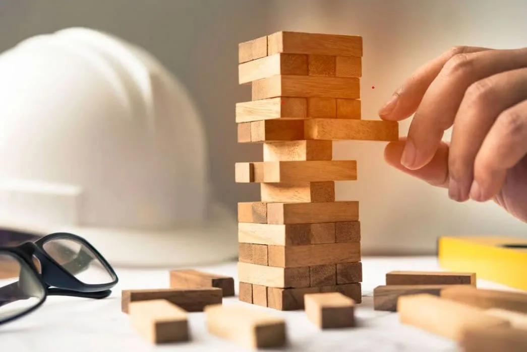 Hand stacking wooden blocks beside a safety helmet – construction quality assurance
