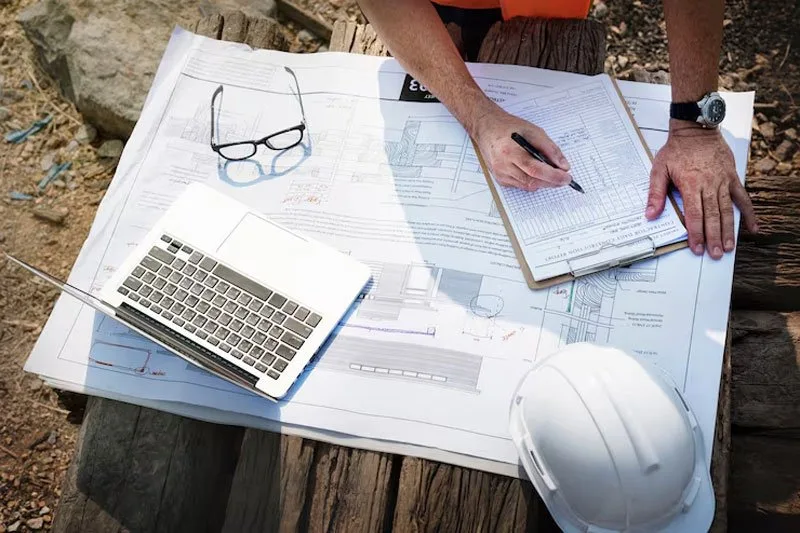 Engineer reviewing building plans with a laptop and safety helmet